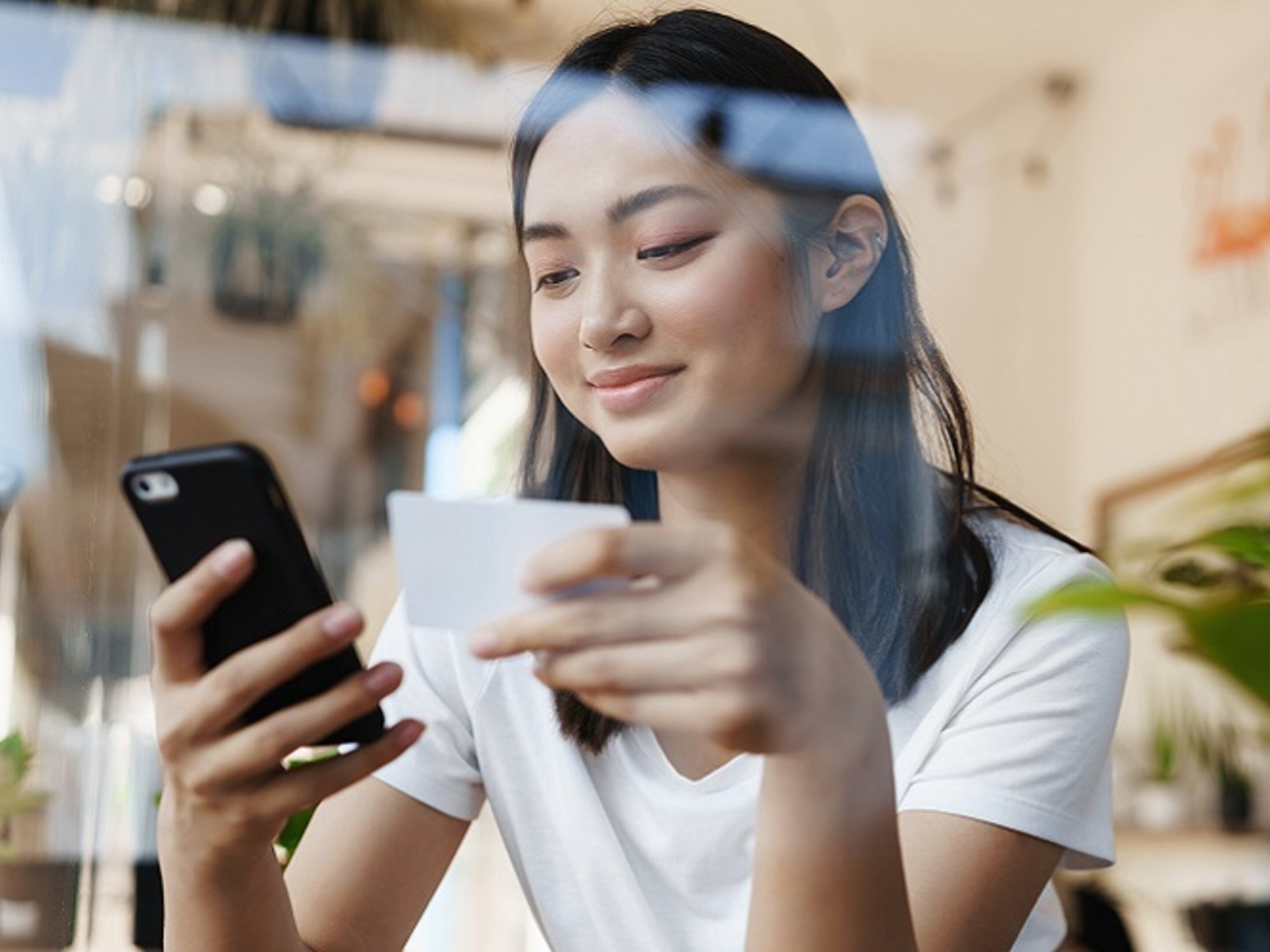 stylish-asian-girl-sitting-cafe-near-window-paying-online-shopping-with-.._cropped